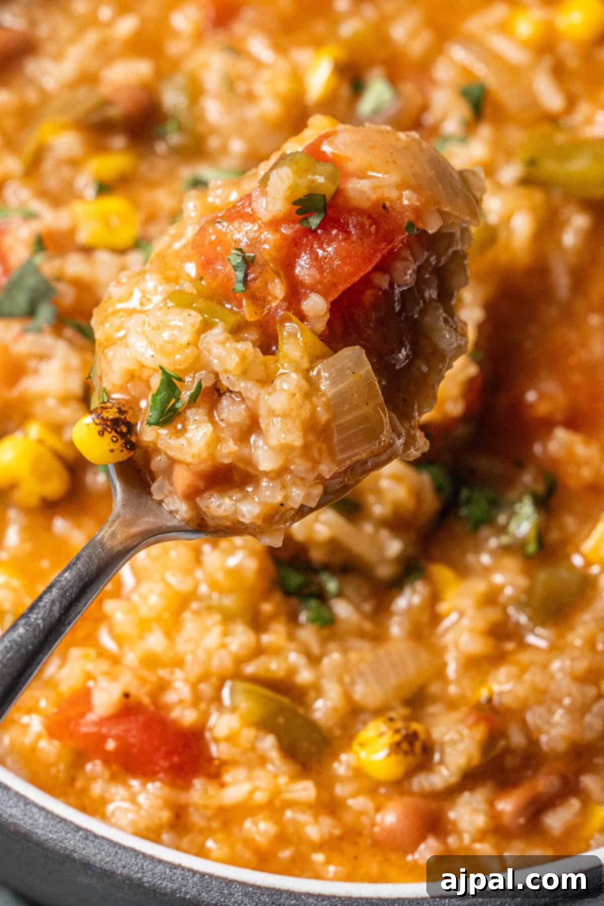 A close-up of a spoonful of thick vegan soup with corn, tomatoes, rice, and herbs held above a pot of hearty rice soup.