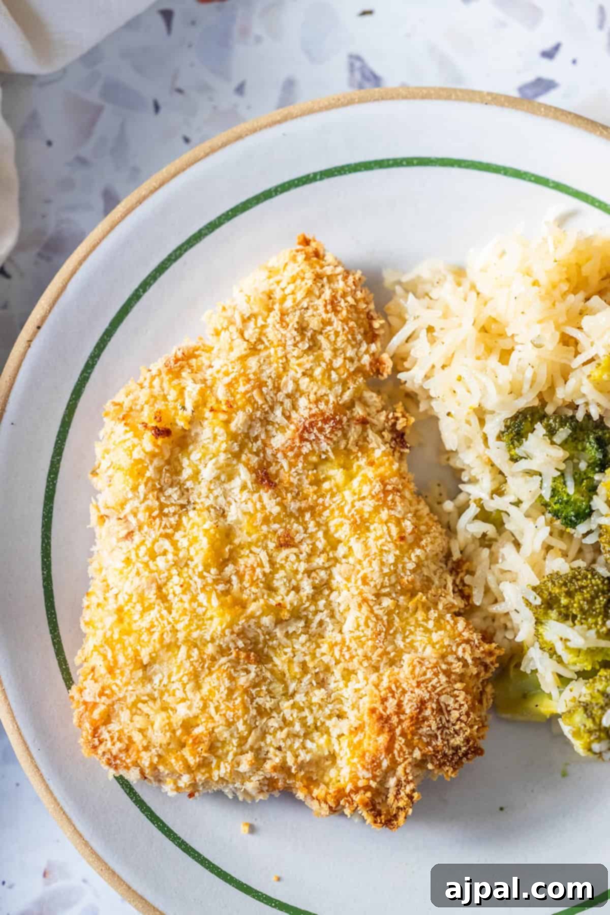 Crispy Oven Pork Cutlets 2 A plate with a perfectly golden-brown baked breaded pork chop, served alongside fluffy rice and vibrant green broccoli, showcasing a balanced and delicious meal.