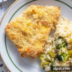 A plate with a crispy baked breaded pork chop, served with white rice and fresh broccoli, an inviting and healthy meal presentation.