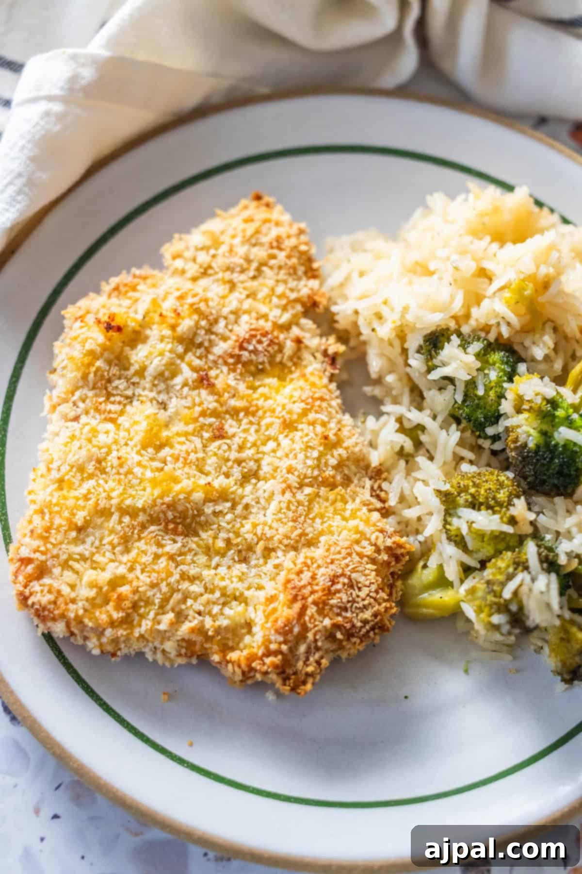 Crispy Oven Pork Cutlets 4 A freshly baked breaded pork chop rests on a white plate with a green rim, accompanied by a generous portion of white rice and tender broccoli florets, emphasizing a wholesome and satisfying dish.