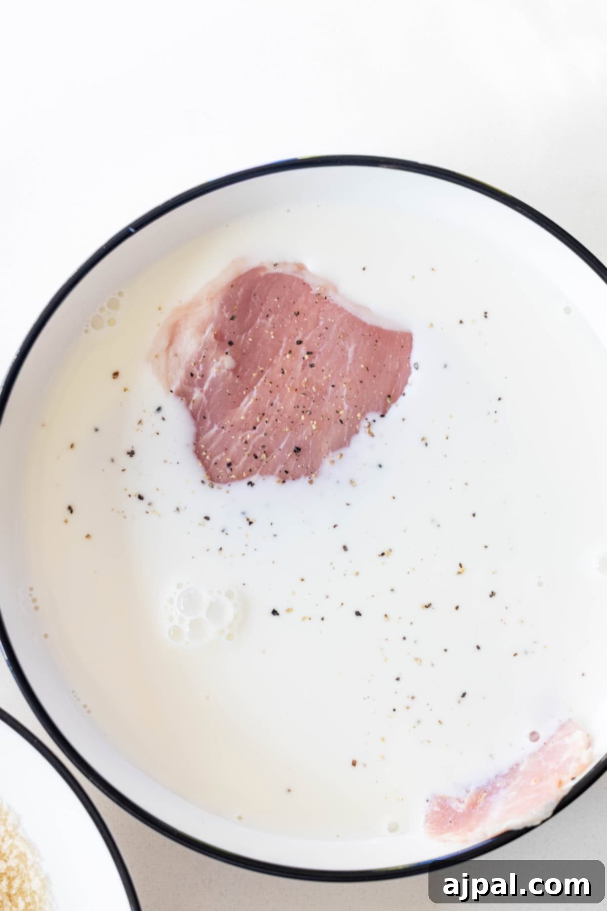 Crispy Oven Pork Cutlets 6 A raw pork chop being submerged in a bowl of milk, an important step for adding moisture and helping the breading adhere to the baked breaded pork chops.