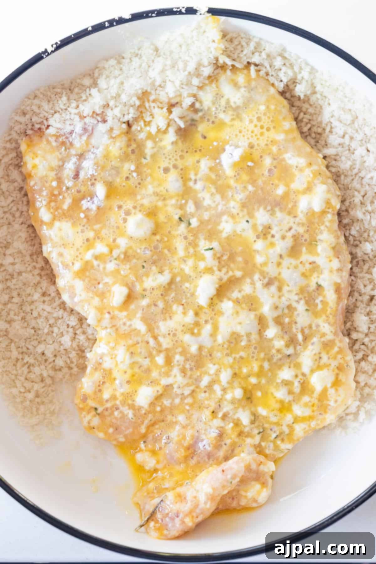 Crispy Oven Pork Cutlets 9 A pork chop freshly coated in egg wash being pressed into a bowl of panko breadcrumbs for thorough coverage, a key step for crispy baked breaded pork chops.