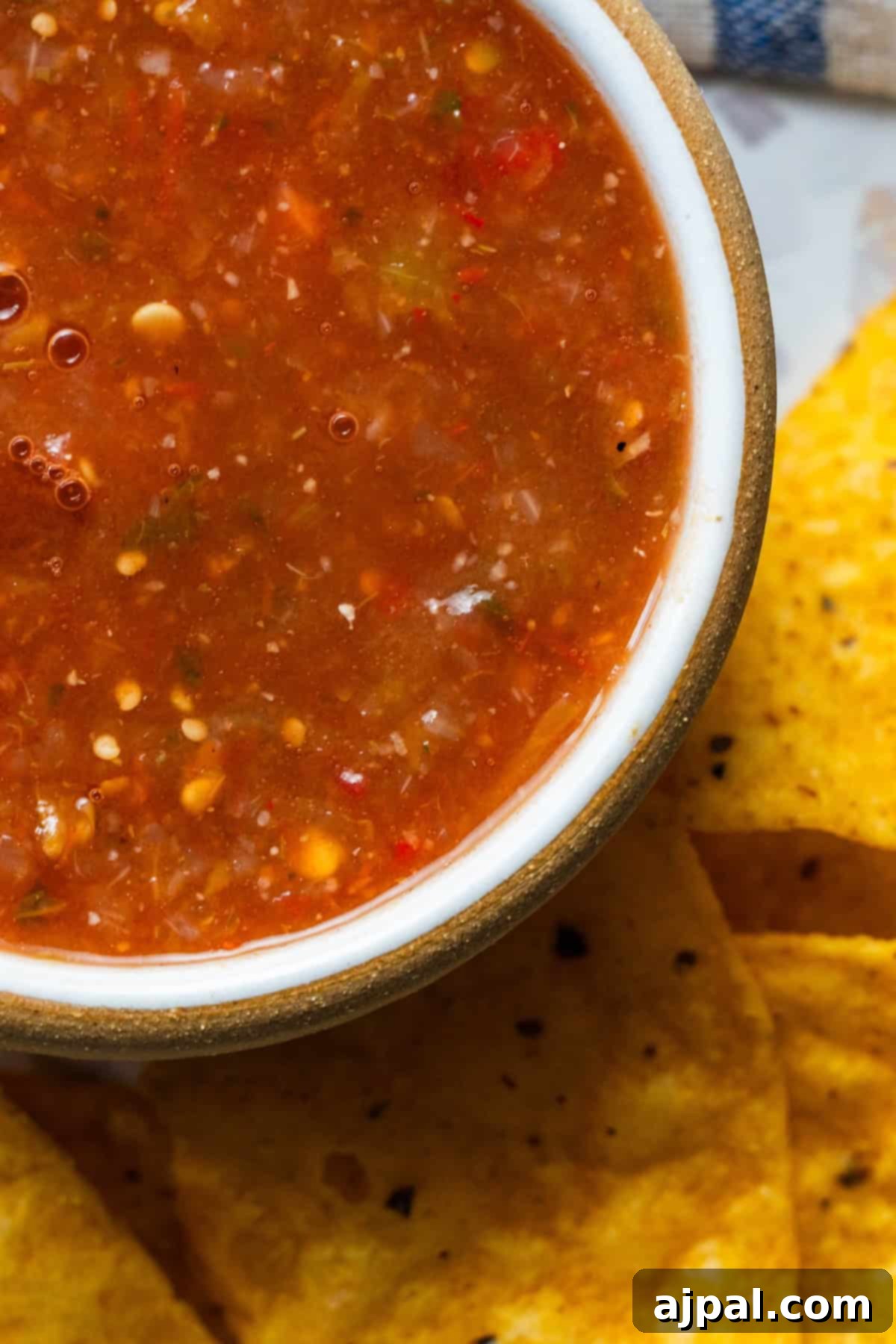 A bowl of red roasted salsa sits next to several yellow corn tortilla chips.