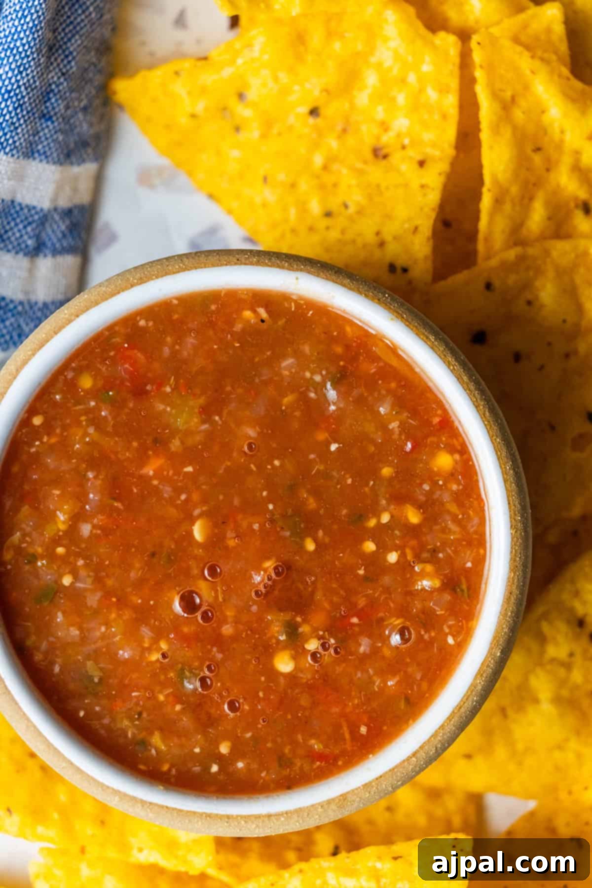 A bowl of vibrant red roasted salsa with visible seeds and spices, surrounded by crispy yellow corn tortilla chips on a plate.