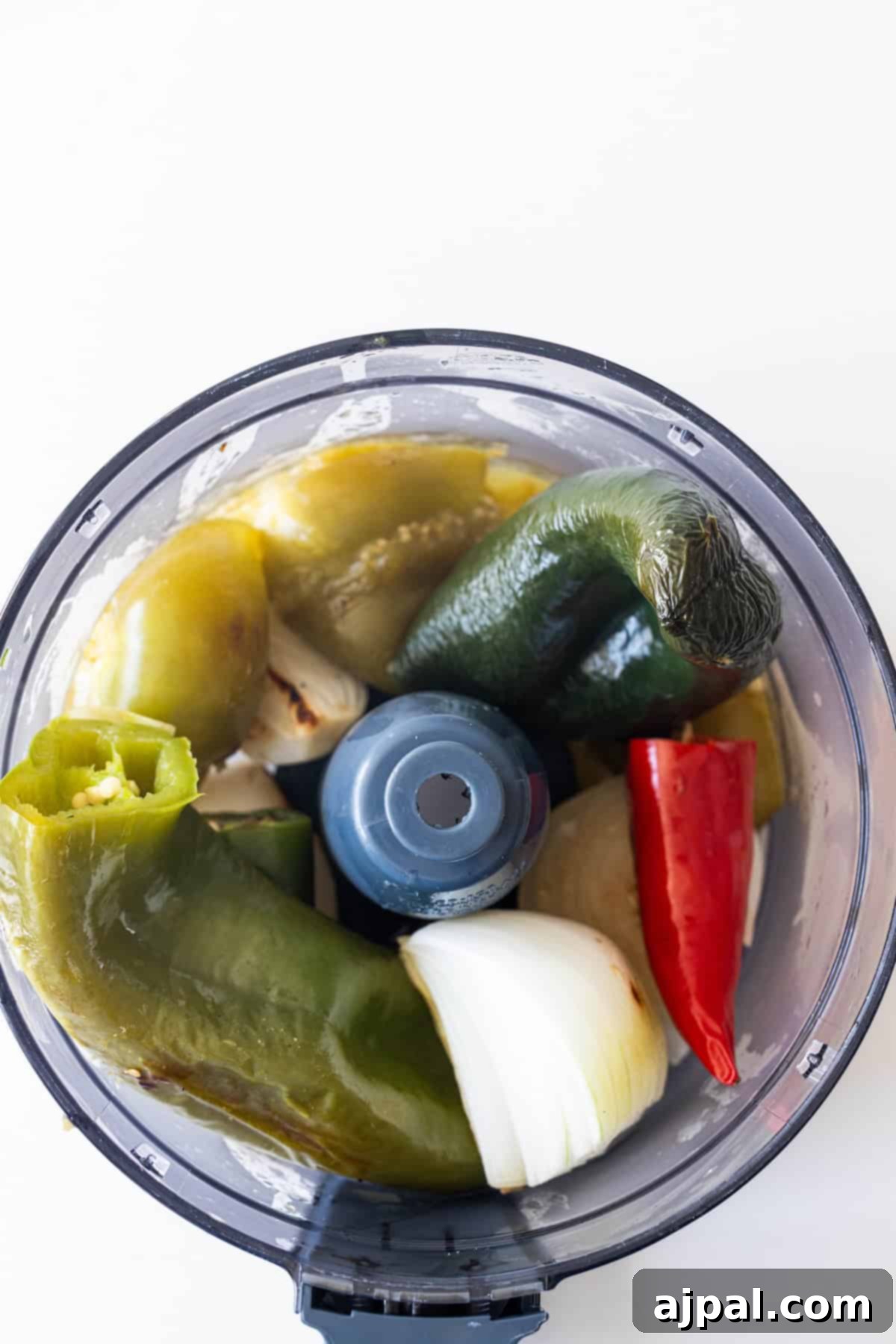 A food processor bowl containing chunks of roasted green and red peppers, pieces of onion, and the makings of a vibrant roasted salsa, viewed from above.