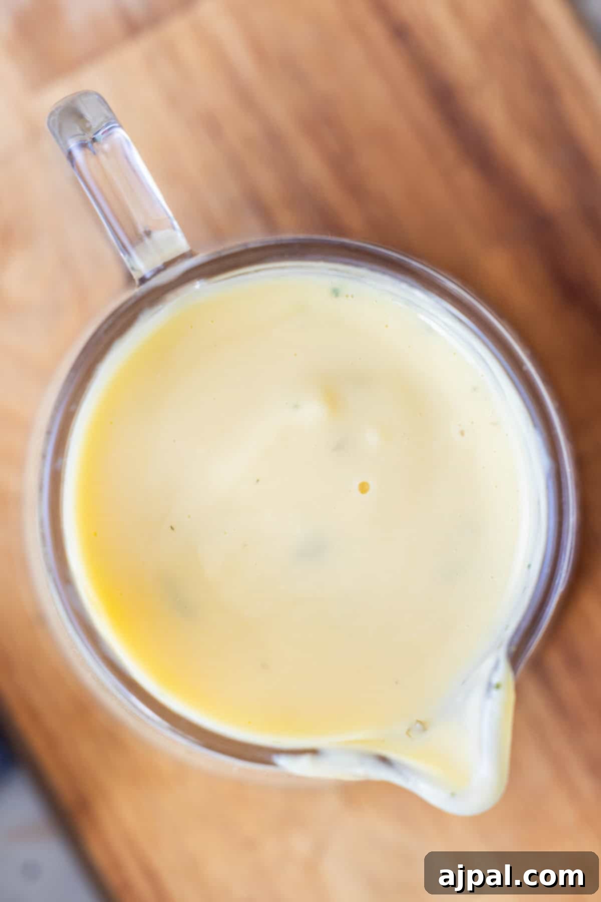 Greek Lemon-Egg Sauce 2 A glass measuring cup filled with creamy yellow Avgolemono Sauce, placed on a wooden surface.