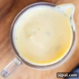 A glass measuring cup filled with creamy yellow sauce, viewed from above, on a wooden surface.