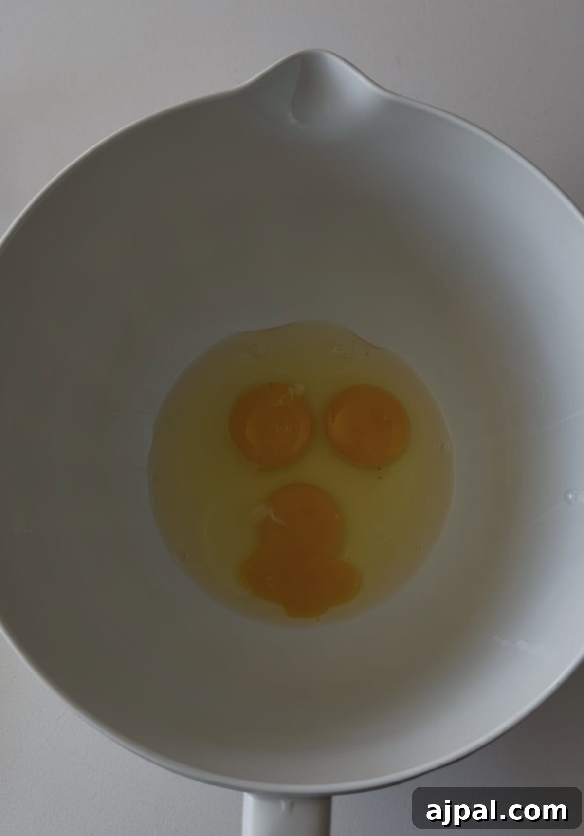 Greek Lemon-Egg Sauce 6 Three raw eggs cracked in a white mixing bowl, their yolks grouped together at the center—perfect beginnings for preparing silky Avgolemono Sauce.