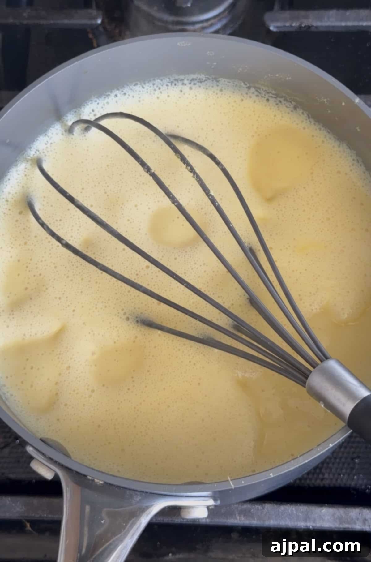 Greek Lemon-Egg Sauce 8 A metal whisk stirs a yellow avgolemono sauce, a classic Greek lemon egg sauce, in a saucepan on a stove.