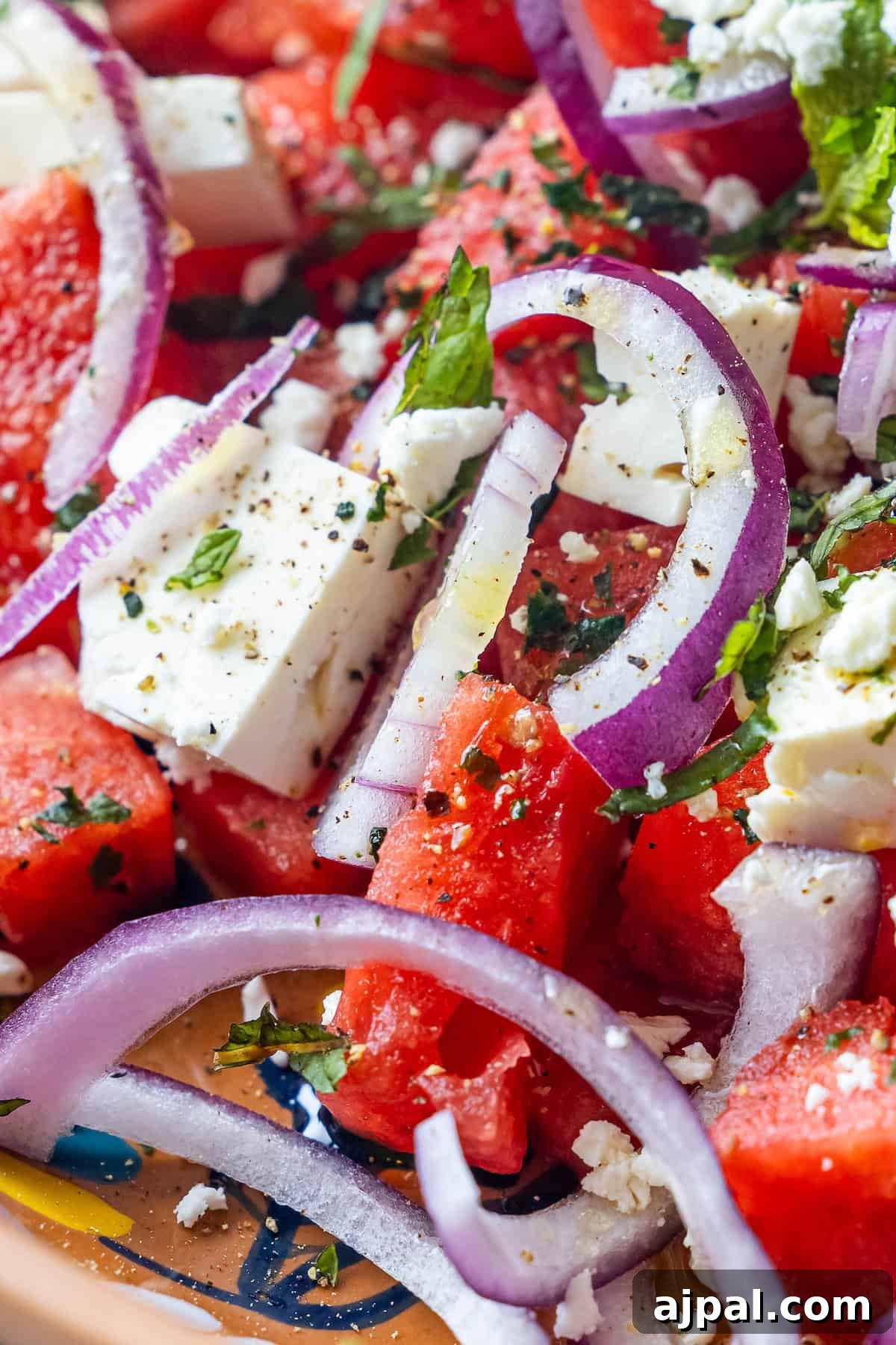Close-up of a Watermelon Feta Salad with juicy watermelon cubes, feta cheese, sliced red onions, chopped mint and basil, and a sprinkle of black pepper.