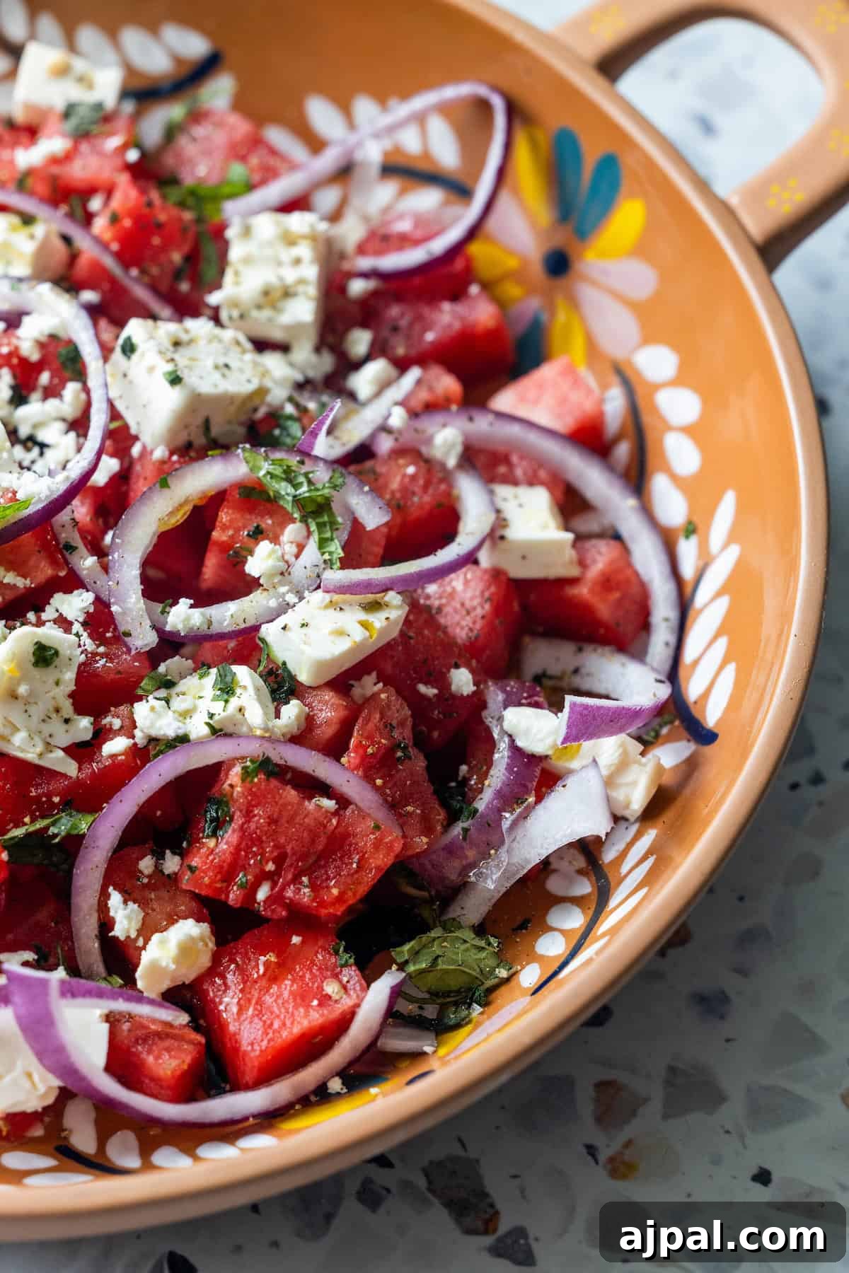 A Watermelon Feta Salad with juicy watermelon cubes, sliced red onions, feta cheese, and fresh mint and basil, served in a decorative ceramic bowl.