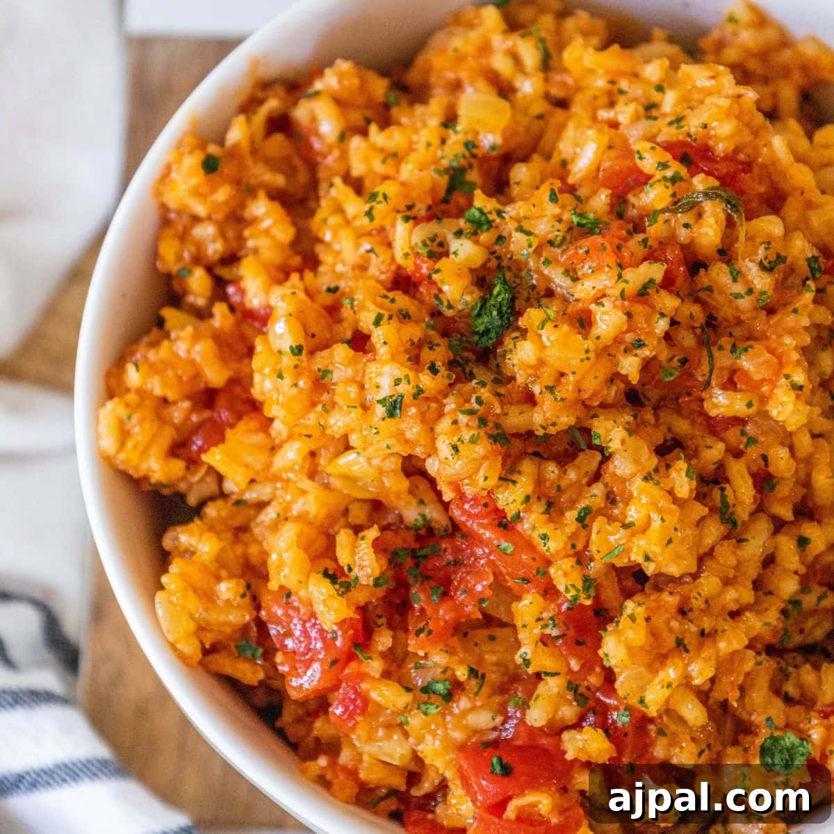 red rice with chunks of tomatoes and chopped cilantro in a white bowl on a table
