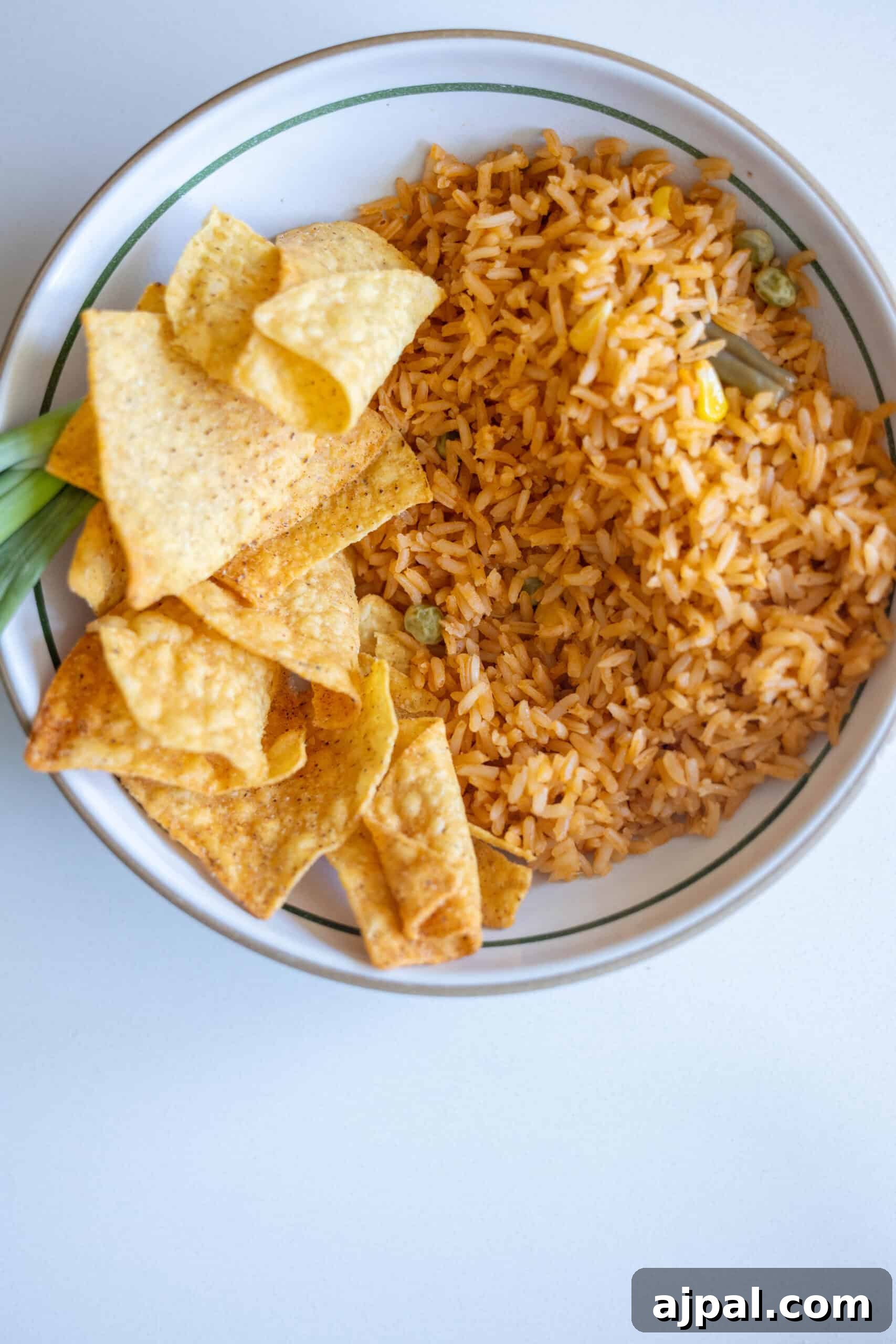 A bowl containing orange-colored rice with green peas and a hint of green chile
