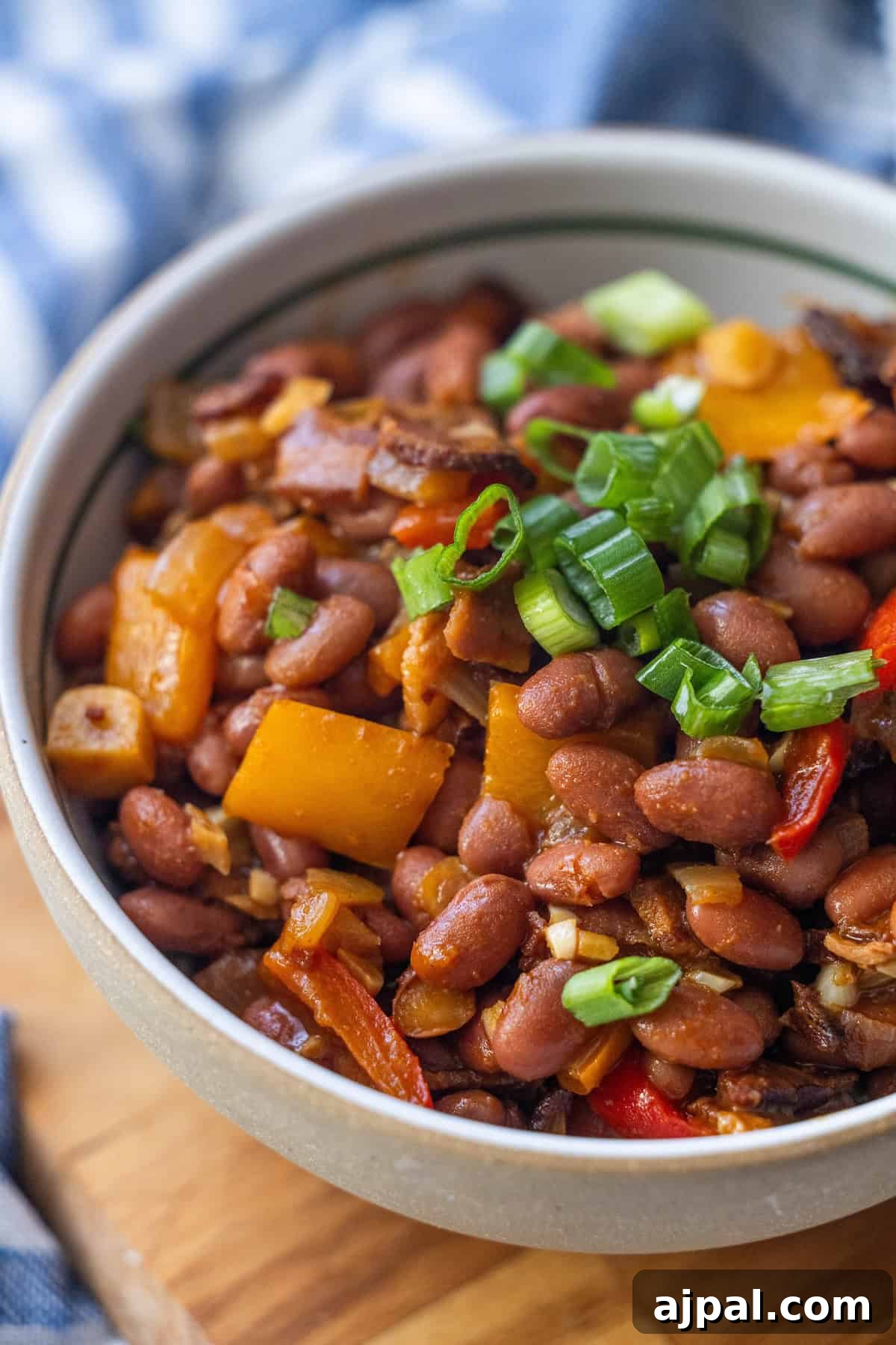 Authentic Mexican Charro Beans Recipe with Bacon and Chiles 2 A bowl of flavorful Mexican beans mixed with chopped bell peppers, green onions, and other vegetables, served on a wooden surface.