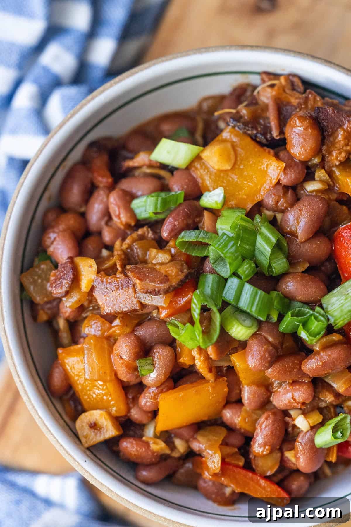 Authentic Mexican Charro Beans Recipe with Bacon and Chiles 4 A bowl of Mexican beans mixed with chopped bell peppers, onions, and garnished with sliced green onions.
