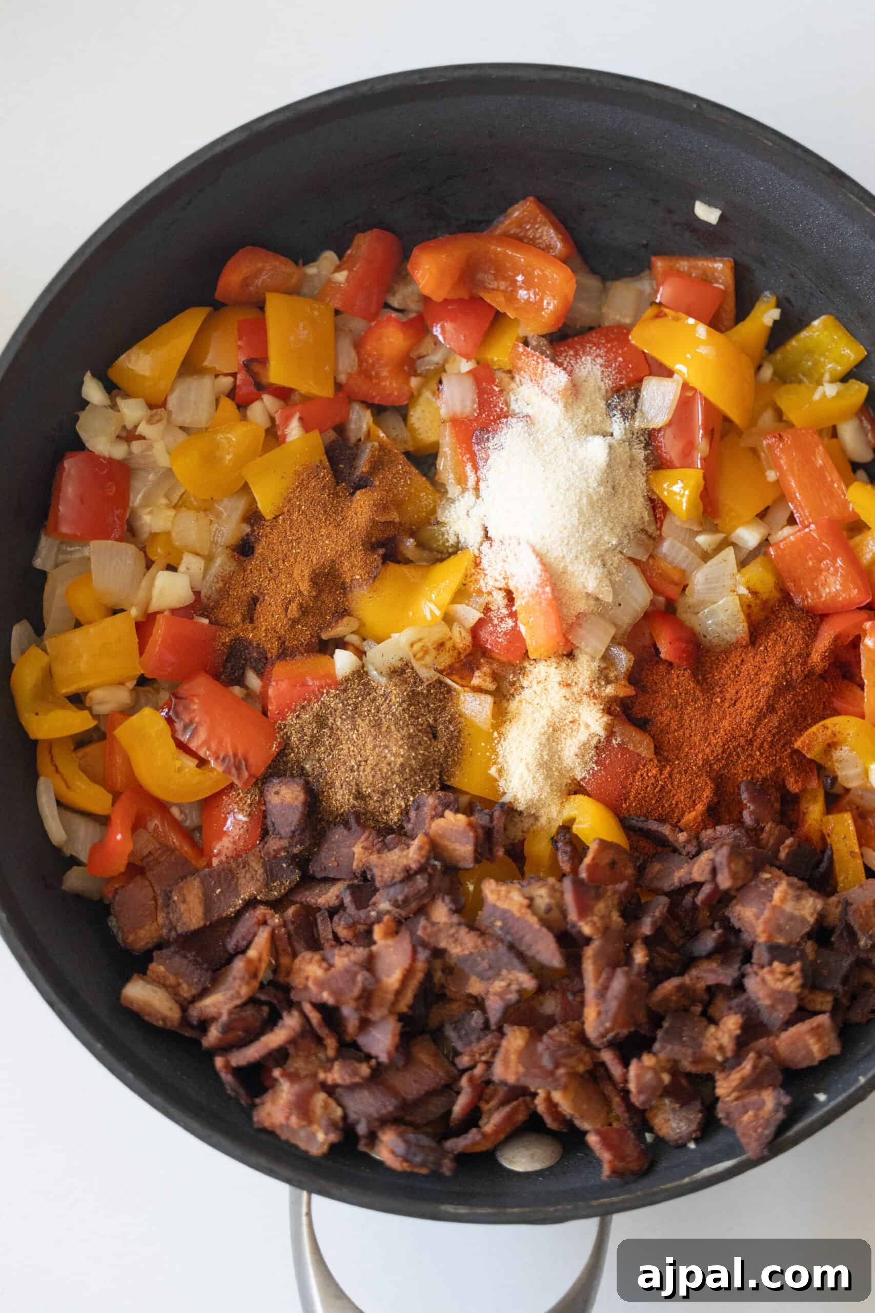 Authentic Mexican Charro Beans Recipe with Bacon and Chiles 6 A skillet containing chopped peppers, onions, crumbled bacon, and spices.
