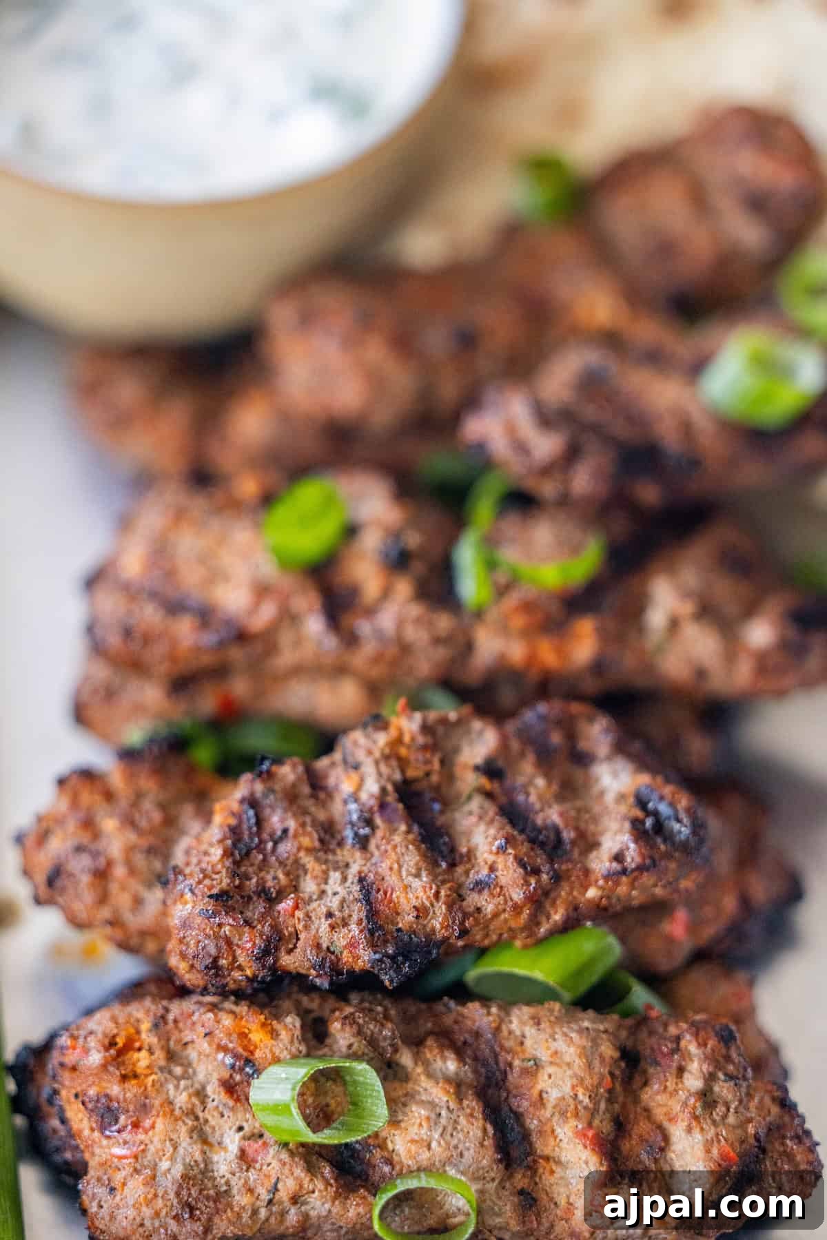Armenian Spiced Lamb Kebabs Recipe with Authentic Seasoning 3 Armenian kebabs featuring spiced meat skewers are garnished with sliced green onions and served with a bowl of white dipping sauce in the background.