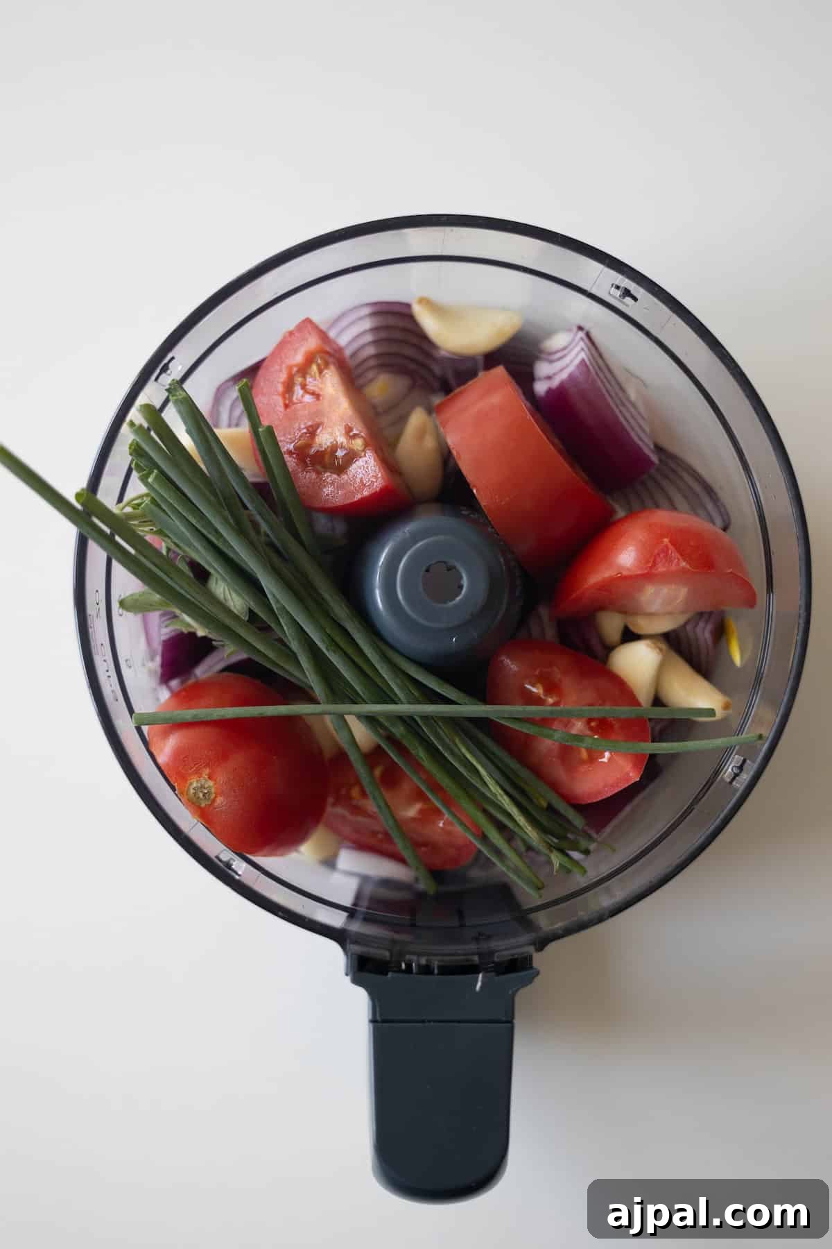 Armenian Spiced Lamb Kebabs Recipe with Authentic Seasoning 6 A food processor bowl filled with chopped red onion, tomatoes, garlic cloves, and fresh chives—perfect for preparing Armenian kebabs or spiced meat mixtures, viewed from above.