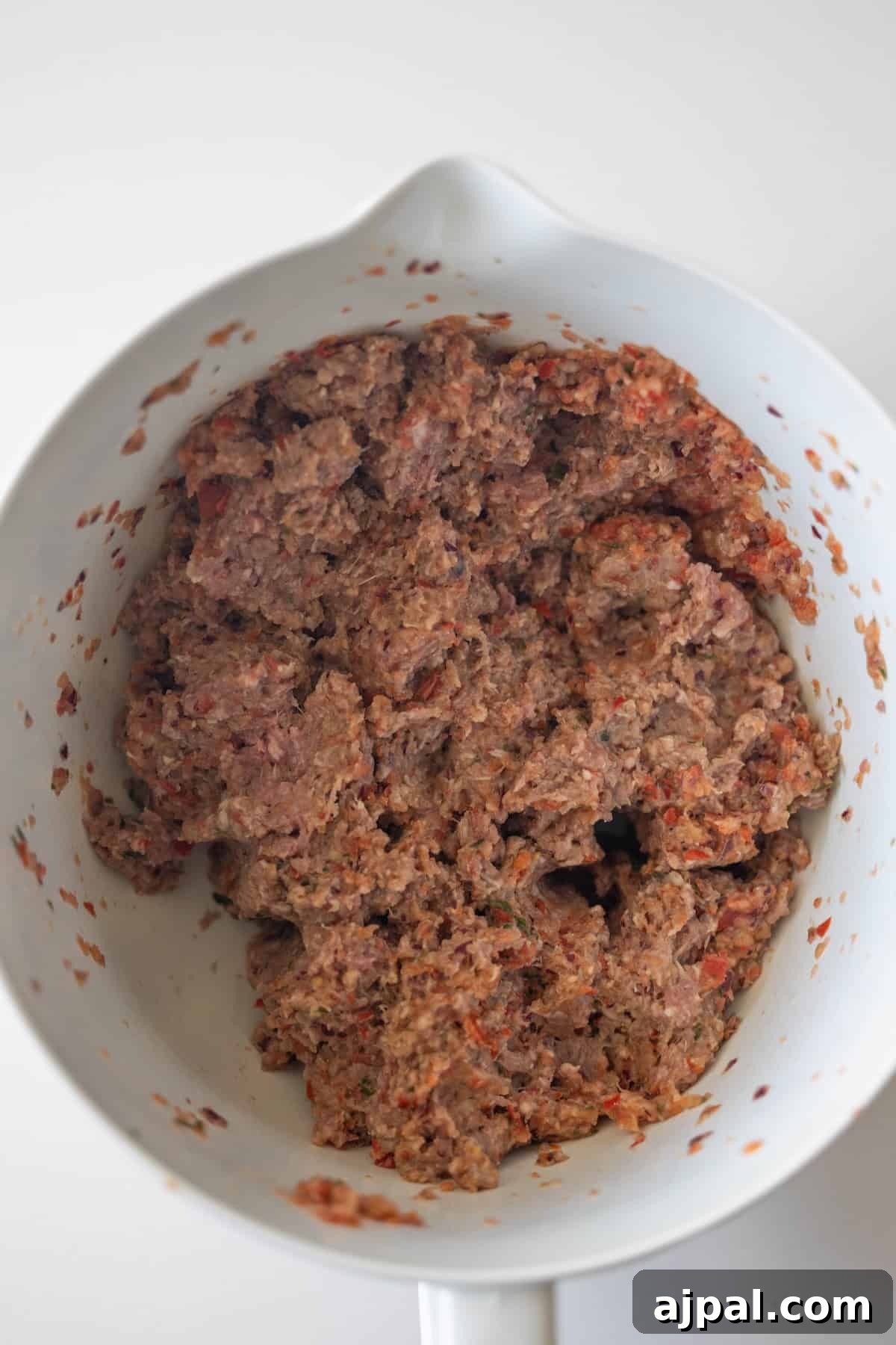 Armenian Spiced Lamb Kebabs Recipe with Authentic Seasoning 8 A white mixing bowl containing Armenian spiced meat and chopped vegetables, perfect for making flavorful kebabs, sits on a white surface.