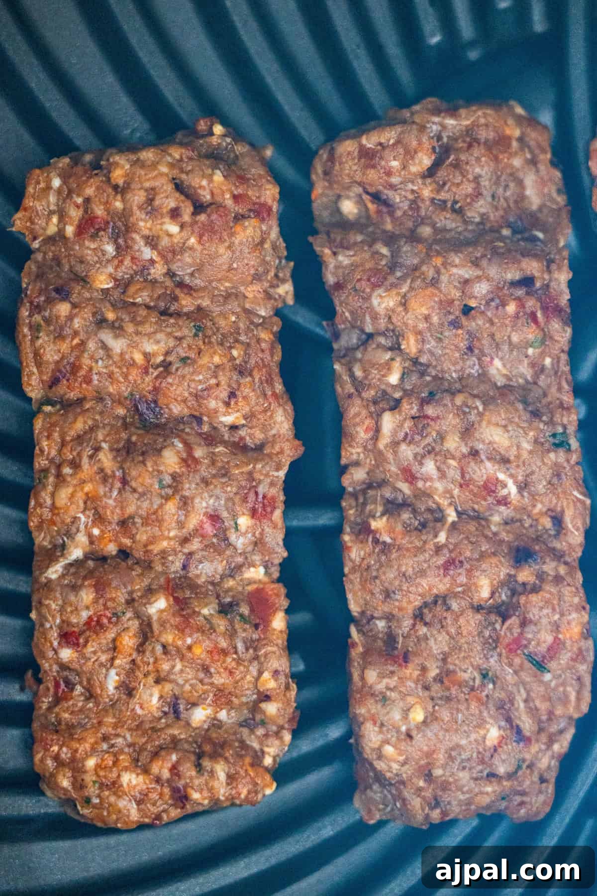 Armenian Spiced Lamb Kebabs Recipe with Authentic Seasoning 10 Two browned Armenian kebabs made of spiced meat with visible herbs and spices are cooking on a black ridged grill surface.