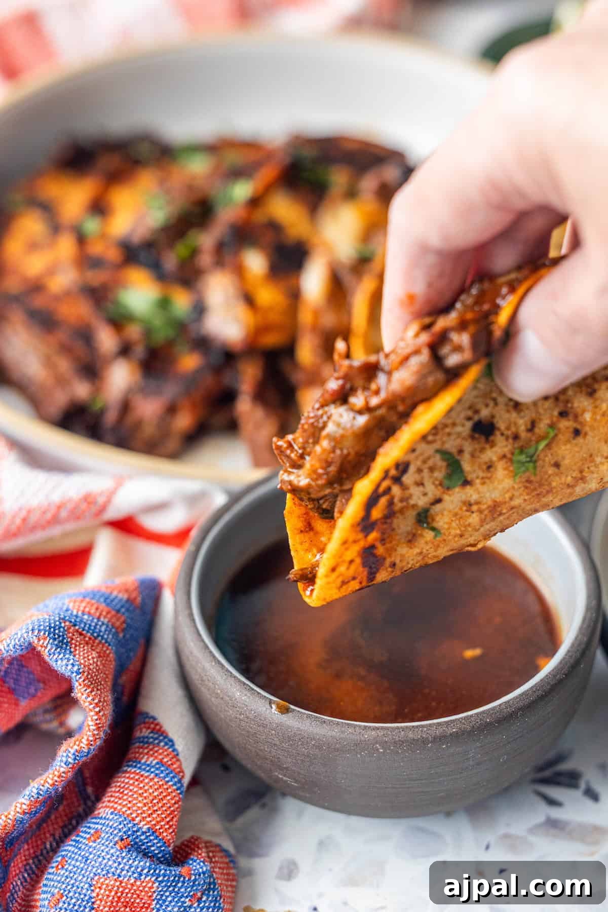 Authentic Birria Tacos Recipe: Juicy Mexican Beef Tacos 5 A hand dips one of the Birria Tacos into a bowl of rich, flavorful broth.