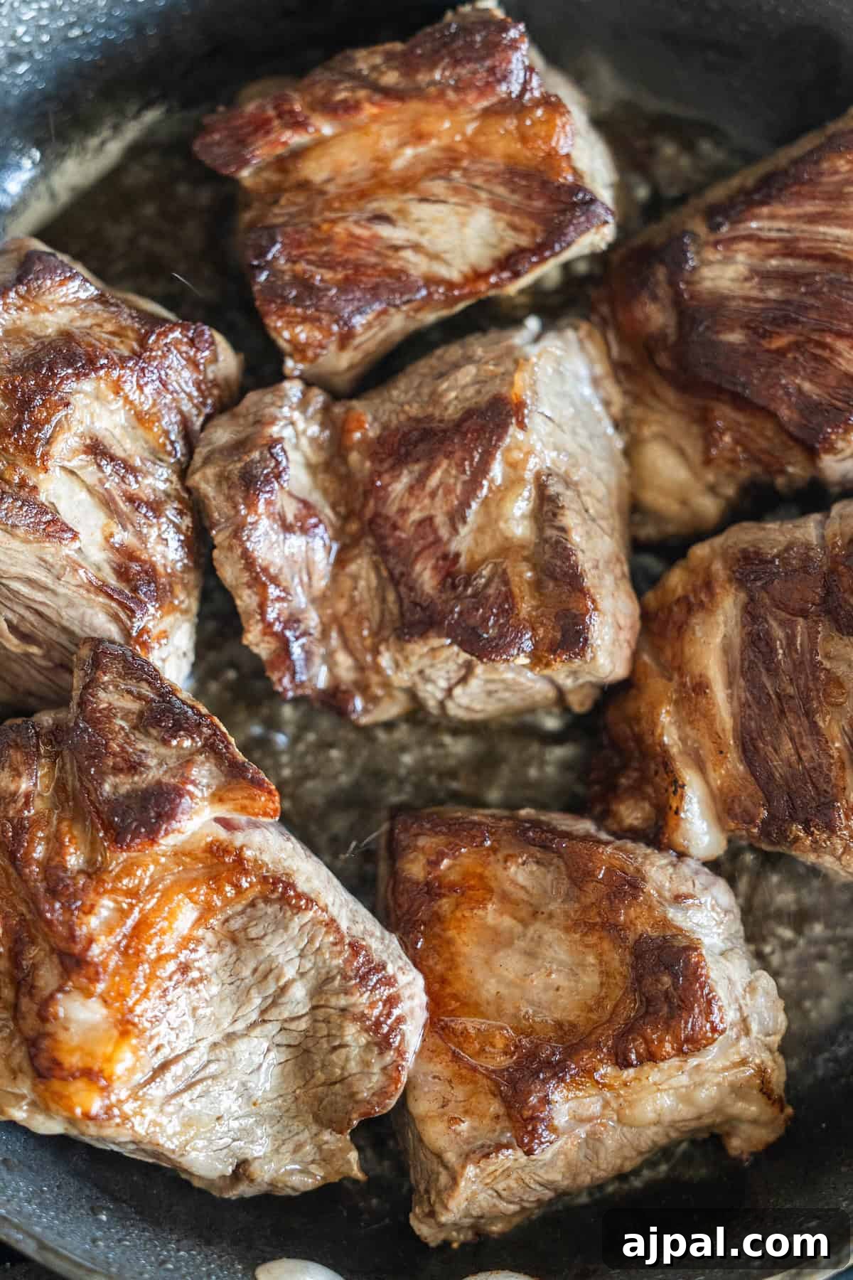 Authentic Birria Tacos Recipe: Juicy Mexican Beef Tacos 6 Several browned beef chunks are being seared in a black skillet.