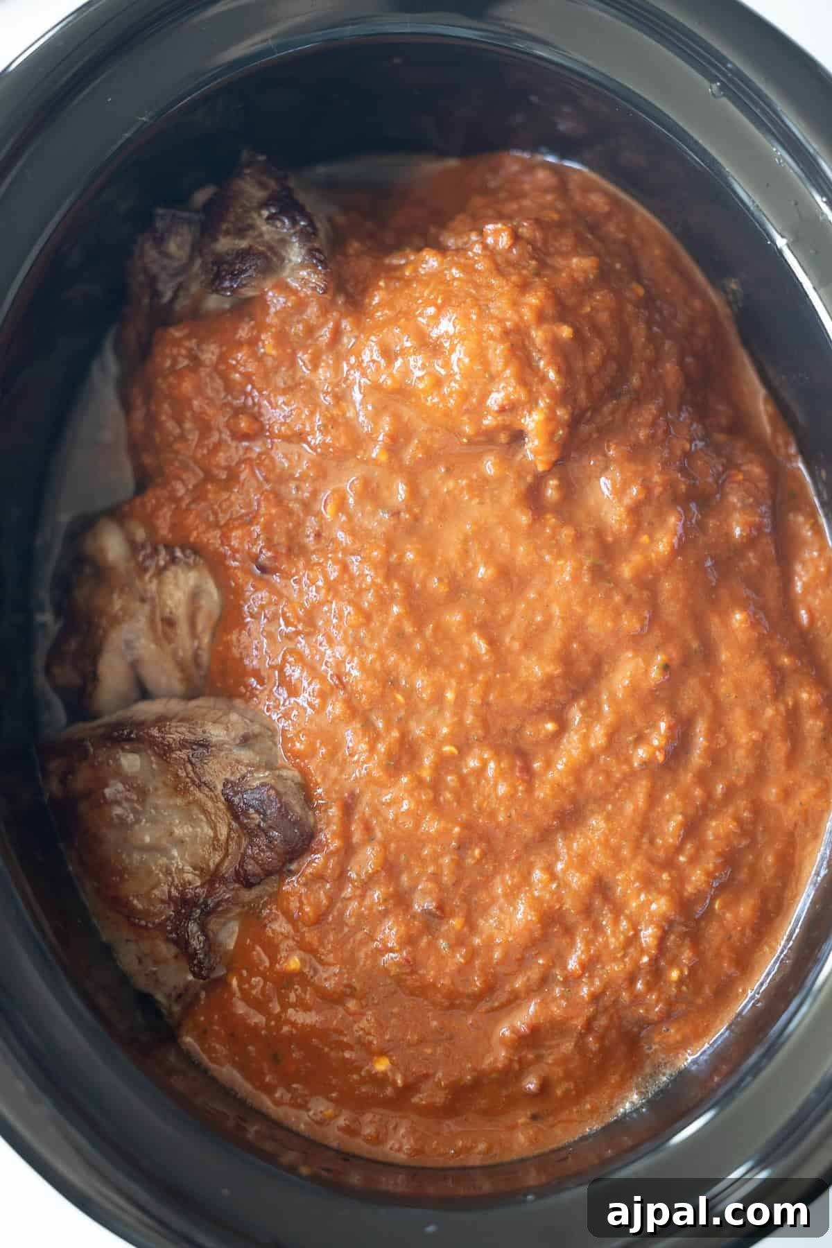 Authentic Birria Tacos Recipe: Juicy Mexican Beef Tacos 8 Slow cooker with browned meat partially covered in a thick red sauce.