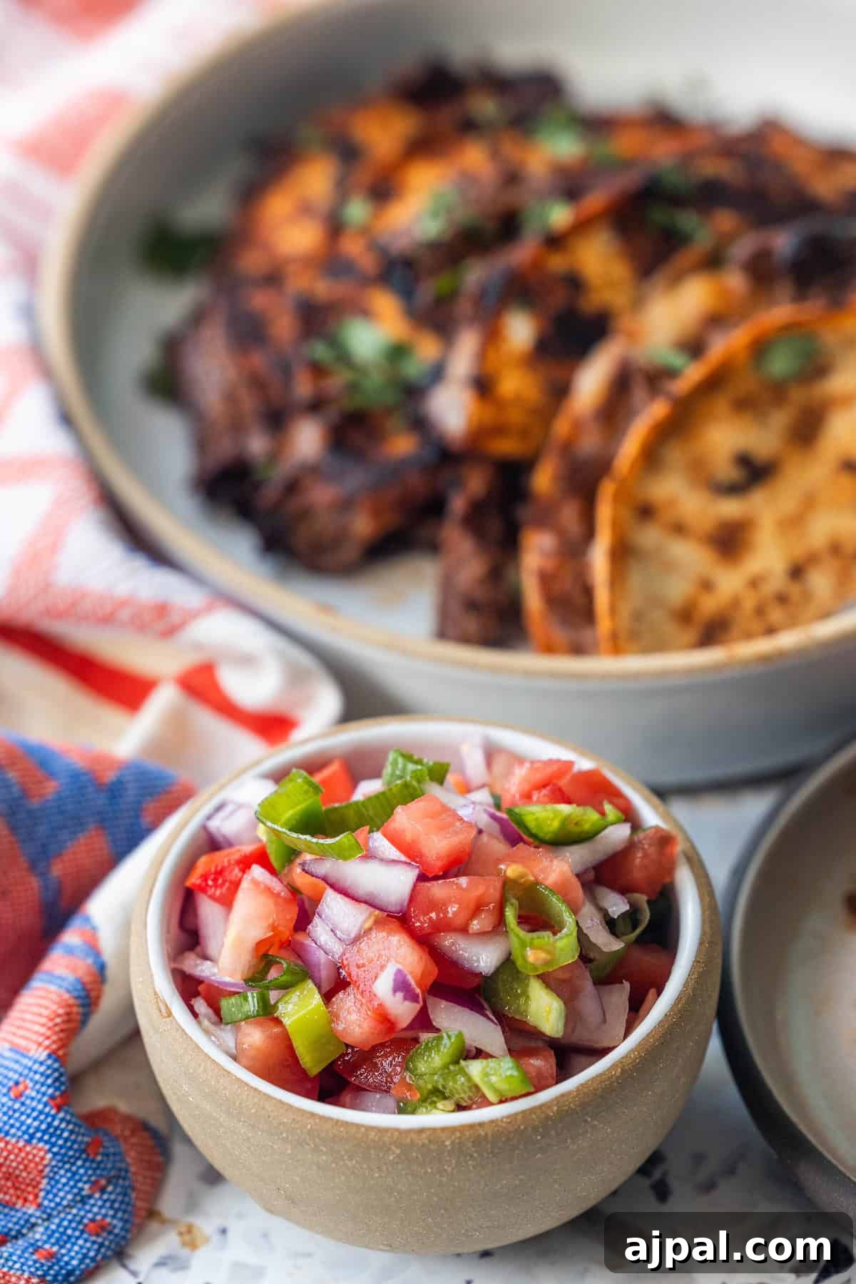 Pico de Gallo Recipe: Fresh Mexican Tomato Salsa 5 A small bowl of fresh salsa with diced tomatoes, onions, and jalapeños in front of a plate of grilled meat and tortillas.