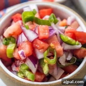 A bowl filled with chopped tomatoes, red onions, and green chili peppers, mixed together for a fresh salsa known as Pico de Gallo.