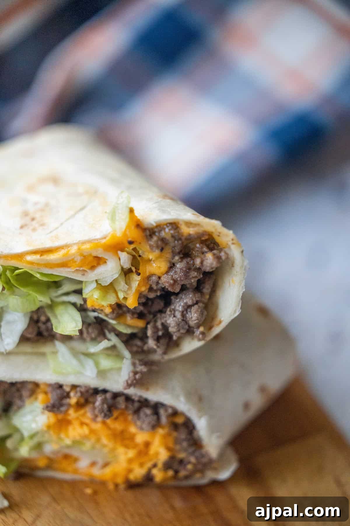 30 Back-to-School Meals That Reheat Perfectly 14 A close-up of easy cheeseburger wraps cut in half, filled with ground beef, shredded cheddar cheese, and lettuce, stacked on a wooden surface.
