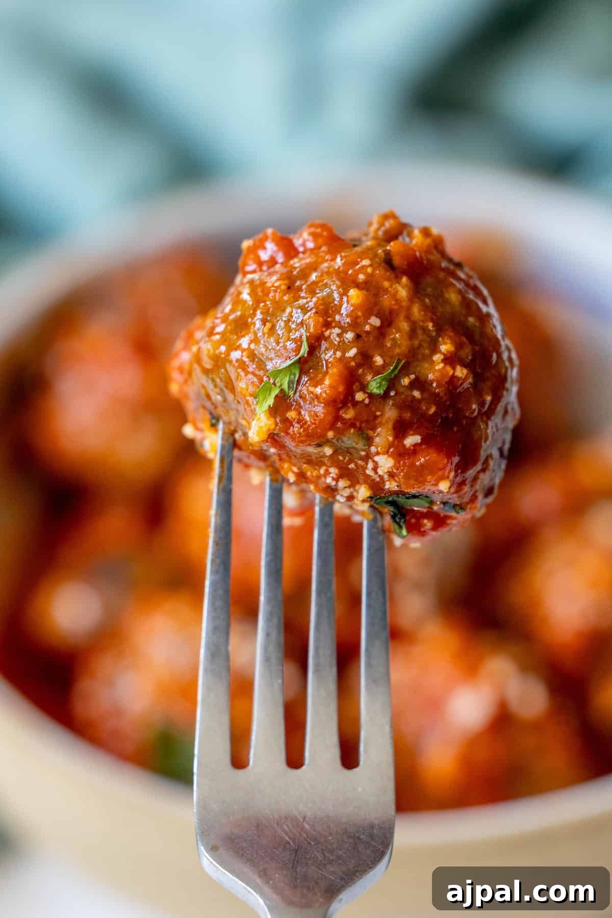 30 Back-to-School Meals That Reheat Perfectly 7 A close-up of a fork holding a meatball covered in tomato sauce with a blurred background of more baked meatballs.