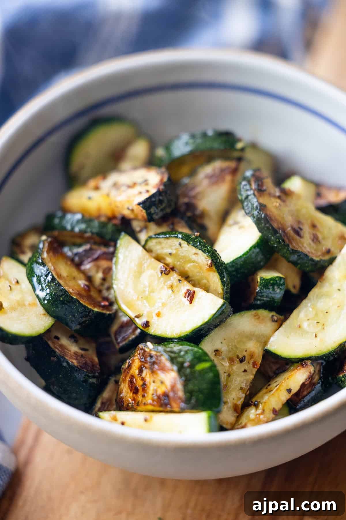 A bowl filled with sliced, sautéed zucchini pieces with visible seasoning, placed on a wooden surface—a simple yet delicious dish that’s perfect for anyone searching for easy zucchini recipes. This Pan-Fried Zucchini is a flavorful addition to your collection of pan fried vegetables.