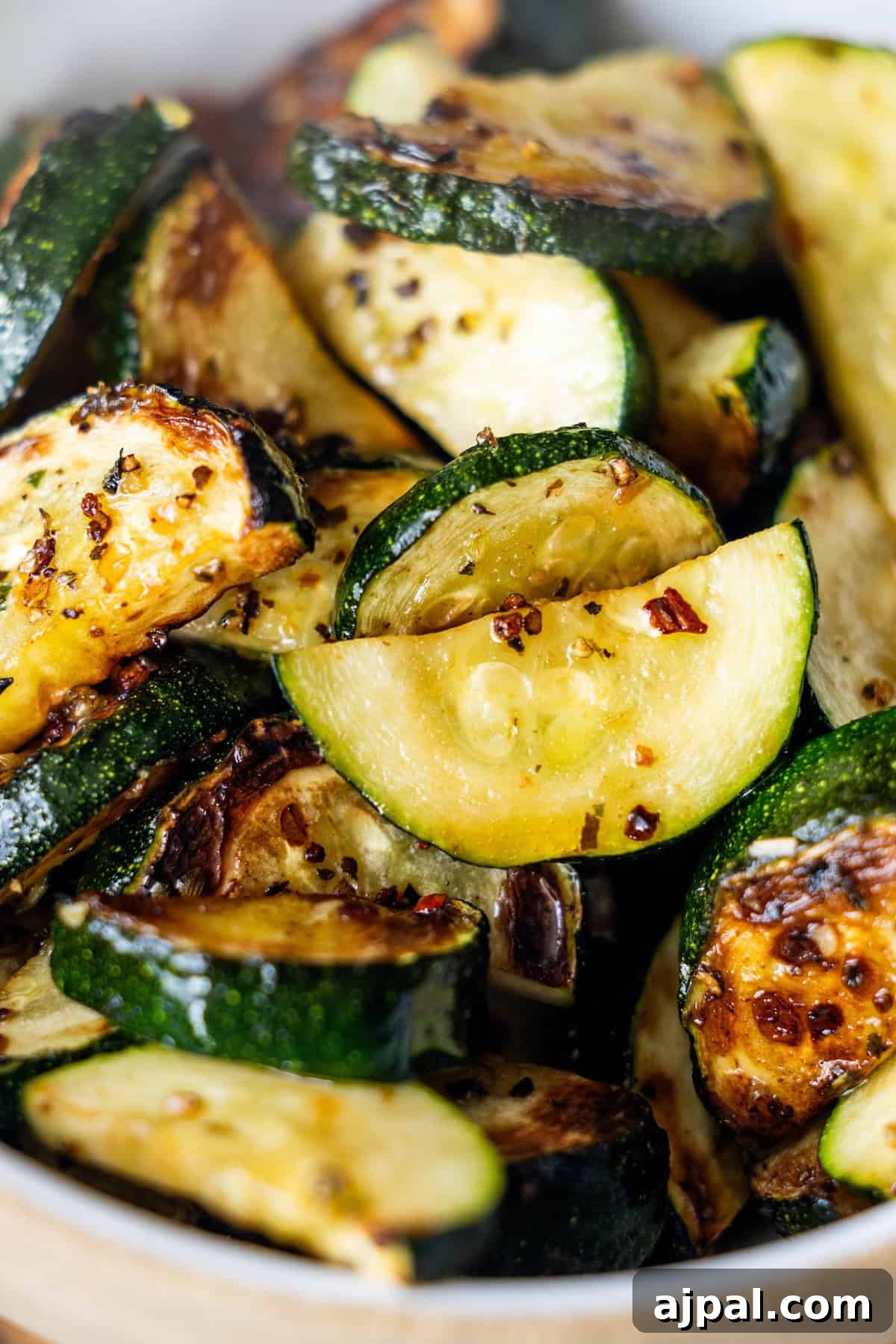 Close-up of pan-fried zucchini slices with browned edges, seasoned with spices and visible red pepper flakes.