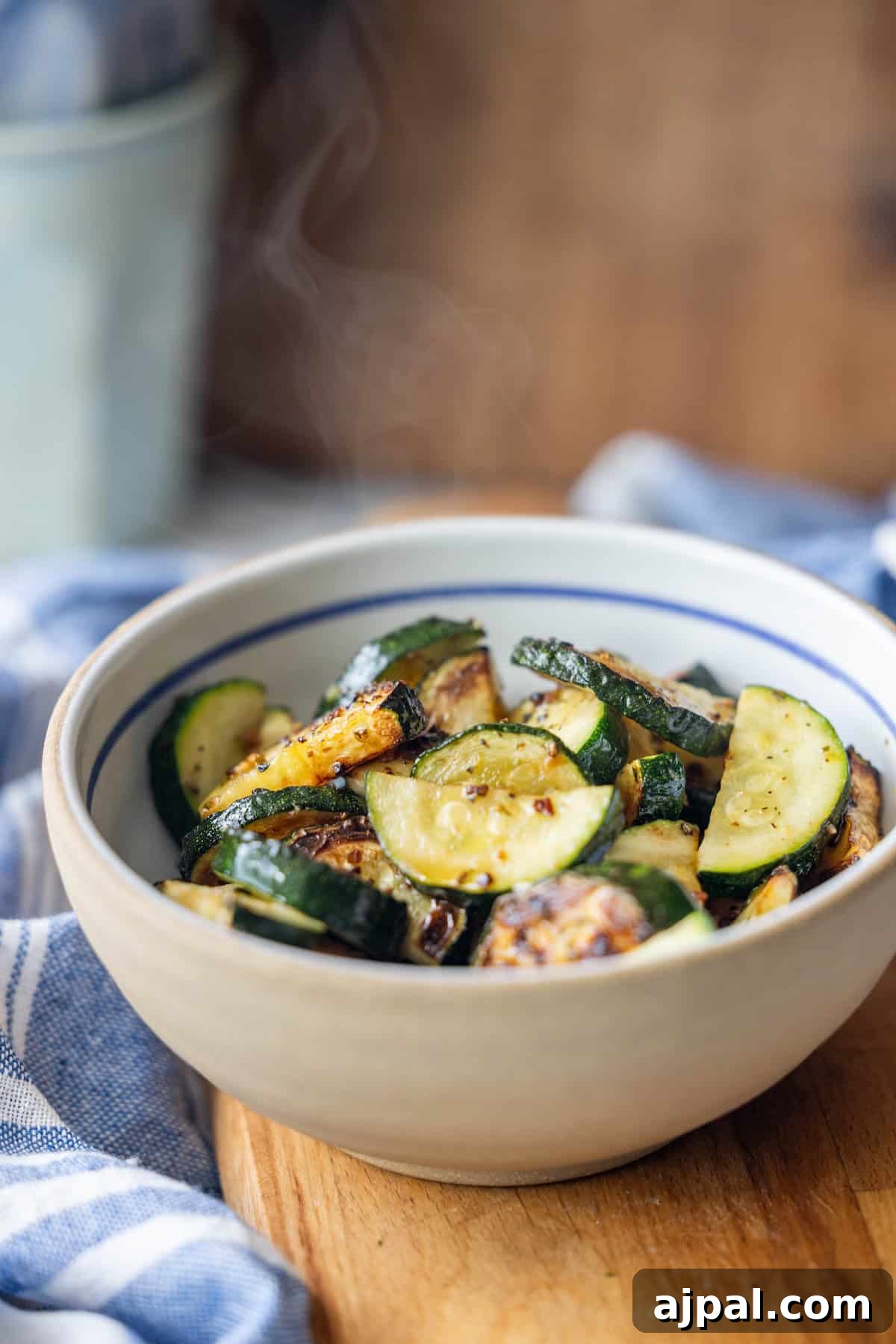 A bowl of pan-fried zucchini slices sits on a wooden surface, with steam rising from the vegetables—an inviting display for anyone seeking a flavorful zucchini recipe.