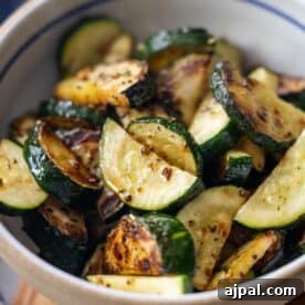 Bowl of roasted zucchini slices, inspired by classic zucchini recipes, seasoned with herbs and spices and showing a slightly charred and golden appearance.